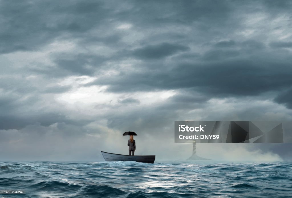 Businesswoman Holding Umbrella Looks At Lighthouse While Stranded On Boat A beacon from a lighthouse beckons a stranded businesswoman holding an umbrella as she stands in a small boat that floats under an ominous sky and choppy waters. Risk Stock Photo