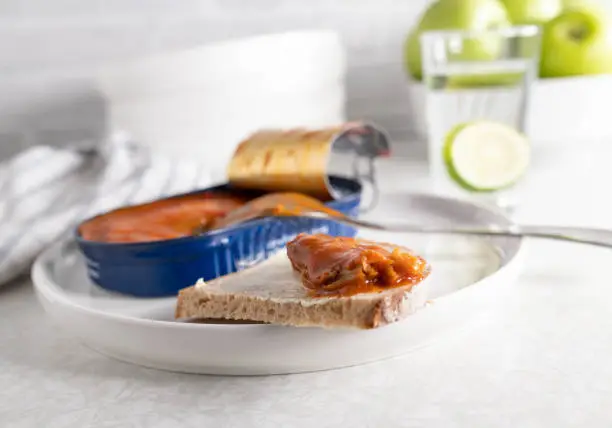 Traditional german bread snack with canned herring with tomato sauce and a slice of buttered bread. Served ready to eat on light kitchen table background.