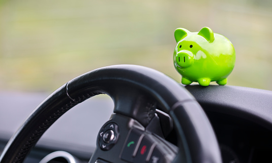 Green piggy bank money box in car interior, vehicle purchase, insurance or driving and motoring cost