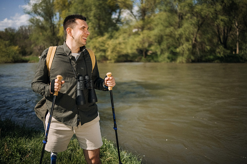 Hiking man with one artificial leg stands by a river in the forest