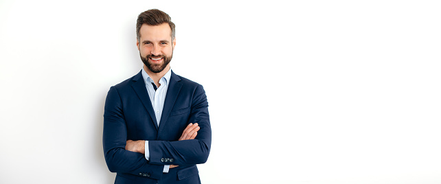 Panoramic portrait of a handsome positive caucasian successful business man in a suit, seo, banker, broker, stand on isolated white background with arms crossed, looks at camera, smiling. Copy-space