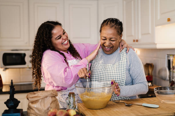 Happy African mother and daughter having fun preparing a homemade dessert stock photo