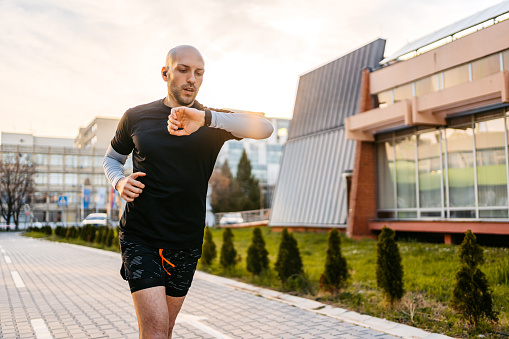 Young athlete checking fitness activity on smartwatch while running outdoors.