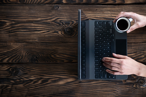 Woman typing on laptop on wooden desk with coffee with space