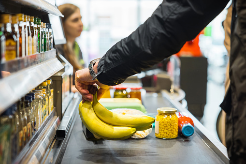 A person putting some bananas and other groceries on the conveyor at a store checkout.
