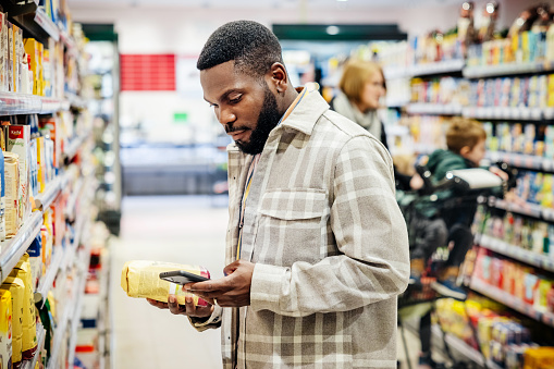 A man using his smartphone and looking up ingredients from a product while grocery shopping in his local supermarket.