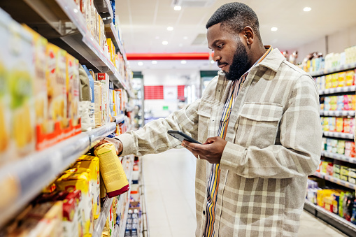 Man Looking At Smartphone While Choosing Items In Supermarket