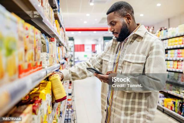 Man Looking At Smartphone While Choosing Items In Supermarket Stock Photo - Download Image Now