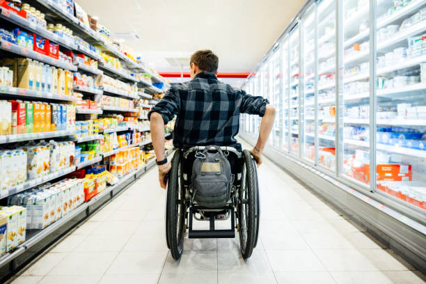 휠체어를 탄 남자는 지역 슈퍼마켓에서 식료품을 쇼핑한다 스톡 사진