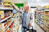 Man Reaching Up To Top Shelf To Take Item While Grocery Shopping