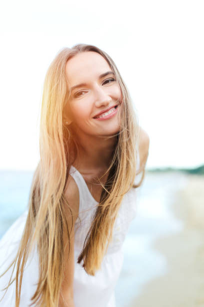 Happy smiling woman in free happiness bliss on ocean beach looking at camera. Portrait of a multicultural female model in white summer dress enjoying nature during travel holidays vacation outdoors. mujer feliz y sonriente en felicidad gratuita en la playa del océano mirando a la cámara. retrato de una modelo femenina multicultural en vestido blanco de verano disfrutando de la naturaleza durante las vacaciones de viaje vacaciones al aire libre