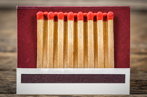 High angle closeup view of a white box of matches and several loose matches scattered on a weathered rustic old wooden bench.