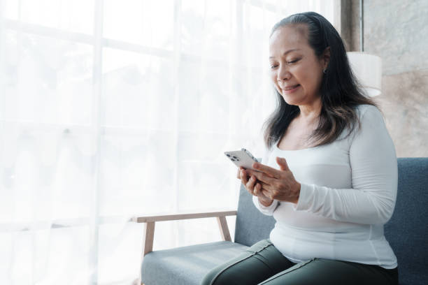 istock Texting on mobile, Happy asian mature woman people relaxing while sitting on a couch 1485797695