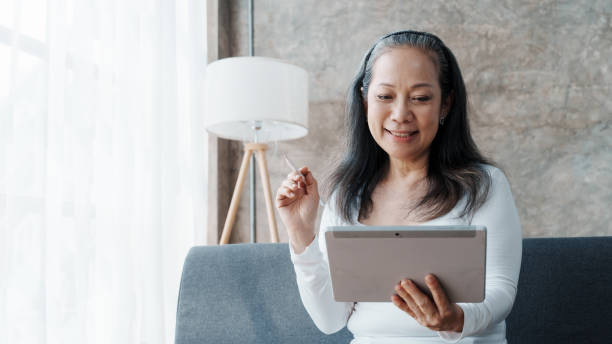 istock Using tablet pc, Happy asian mature woman people relaxing while sitting on a couch 1485797708