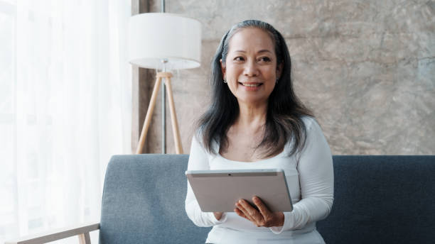 istock Using tablet pc, Happy asian mature woman people relaxing while sitting on a couch 1485797717