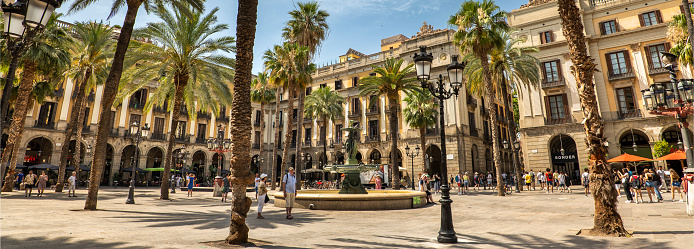 Barcelona, Spain - June 17, 2022:  Plaça Reial or Royal Plaza is a public square with an ornate fountain and palm trees in the Gothic Quarter off of La Rambla in Barcelona Catalonia Spain.  It is a popular tourist attraction at night with many restaurants and nightclubs