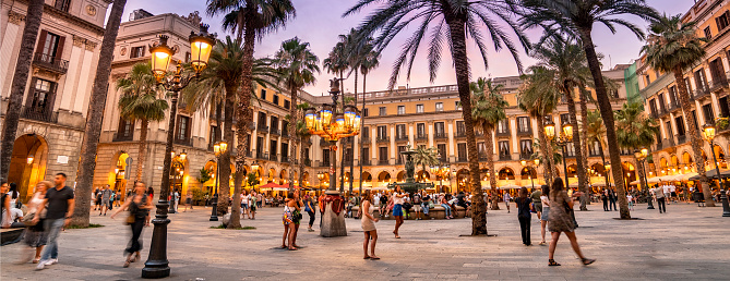 Barcelona, Spain - June 17, 2022:  Plaça Reial or Royal Plaza is a public square with an ornate fountain and palm trees in the Gothic Quarter off of La Rambla in Barcelona Catalonia Spain.  It is a popular tourist attraction at night with many restaurants and nightclubs