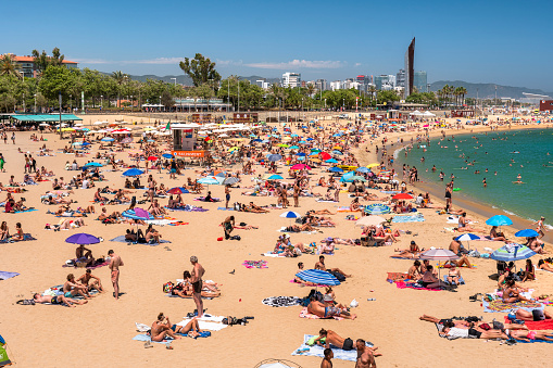 Barcelona, Spain - June 11, 2022:  Crowds of people relax and tan in the hot sun on the sand shores of the Balearic Sea on Barceloneta beach in Barcelona Catalonia Spain