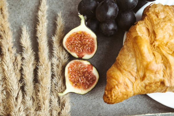 Autumn attributes. Croissant, dark grapes, book and figs on the grey table. Gold October