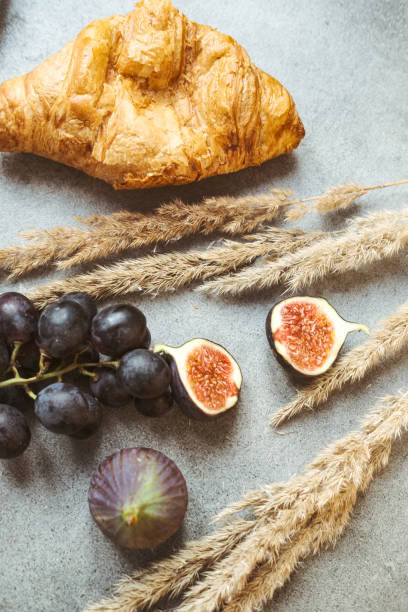 Autumn attributes. Croissant, dark grapes, book and figs on the grey table. Gold October