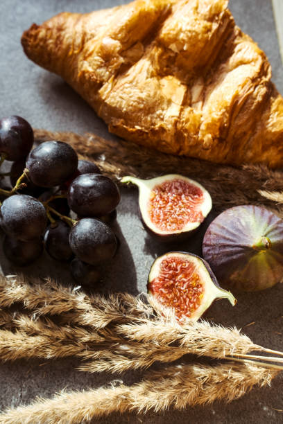 Autumn attributes. Croissant, dark grapes, book and figs on the grey table. Gold October