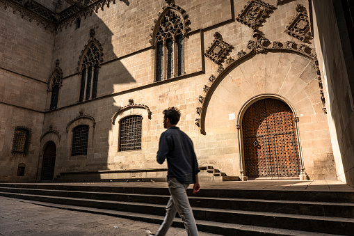 Barcelona, Spain - June 17, 2022:  Man walks by a old historic door of the Barcelona Cathedral on the narrow cobblestone streets in the Gothic quarter of Catalonia Spain