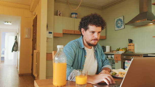 istock Guy dressed in denim shirt gets lunch and works on laptop while sitting in the kitchen 1485808172