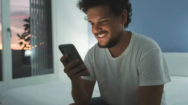 Photo of Guy is sitting on the bed in the bedroom, watching video, movie on mobile phone