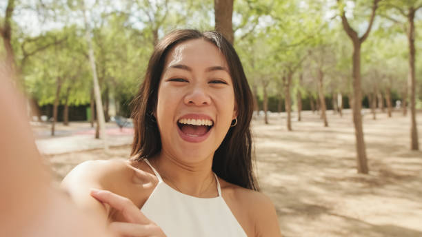 istock Smiling brunette girl dressed in white top and jeans, taking selfie on mobile phone while standing in city park 1485809055
