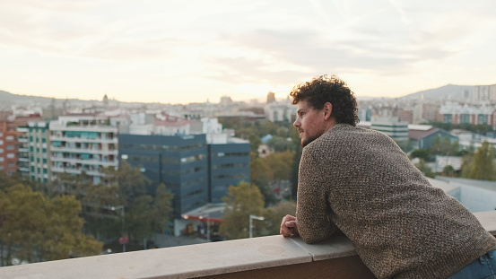 Guy looks at the city from the balcony, enjoys the beautiful view