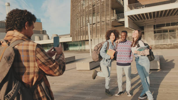 istock Young cheerful people make a joint photo. Group of students smiling while looking at mobile phone camera while standing outside 1485809221