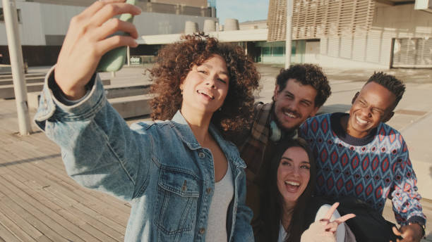 istock Young cheerful people make a joint selfie. Group of students smiling while looking at mobile phone camera while standing outside 1485809354