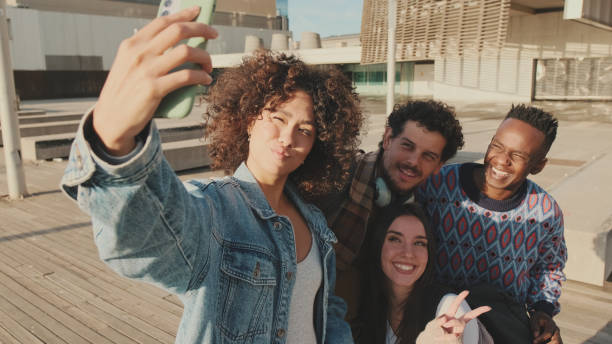 istock Young cheerful people make a joint selfie. Group of students smiling while looking at mobile phone camera while standing outside 1485809359