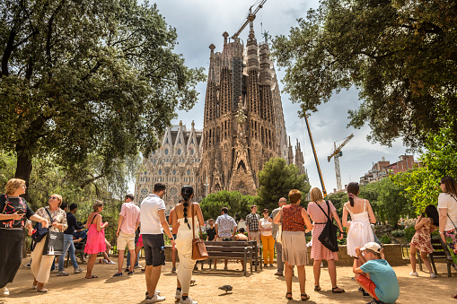 Barcelona, Spain - June 14, 2022:  Tourist crowd admires the architectural detail of the gothic Art Nouveau church spires of the Sagrada Familia basilica in the Eixample district of Barcelona Catalonia Spain