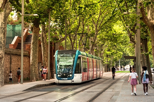 Barcelona, Spain - June 14, 2022:  City streetcar train rides down the tree lined tracks near Parc de la Ciutadella in El Born district of Barcelona Catalonia Spain