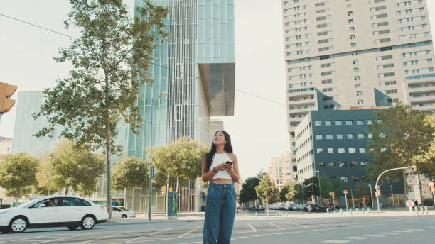 istock Cute happy girl dressed in white top and jeans, uses map application on mobile phone while standing on modern city background 1485809568