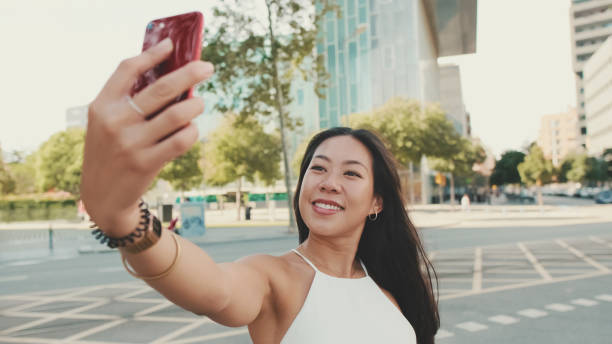 istock Cute happy girl dressed in white top and jeans makes selfie on mobile phone while standing on modern city background 1485809631