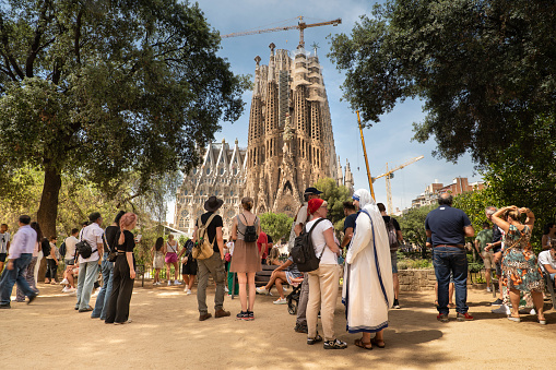 Barcelona, Spain - June 16, 2022:  Tourist crowd admires the architectural detail of the gothic Art Nouveau church spires of the Sagrada Familia basilica in the Eixample district of Barcelona Catalonia Spain