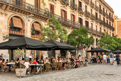 Barcelona, Spain - June 12, 2022:  People sit and socialize on the many outdoor patios cafes, restaurants and bars of the tree lined cobblestone streets and plazas in the Gothic Quarter district in the historic old town of Barcelona Catalonia Spain