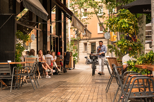 Barcelona, Spain - June 14, 2022:  People sit and socialize on the many outdoor patios cafes, restaurants and bars of the tree lined cobblestone streets and plazas in the Gothic Quarter district in the historic old town of Barcelona Catalonia Spain