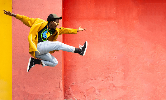 African-American man jumping high in the air with his arms outstretched  and one leg kicking against a colorful orange background