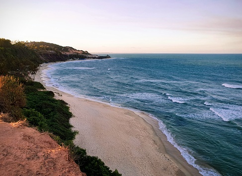 The landscape of Praia do Amor, located in Pipa beach, Tibau do Sul, Rio Grande do Norte, Brazil. Blue sea and the sky with sunset colors. Cliffs and green vegetation. Touristic place.