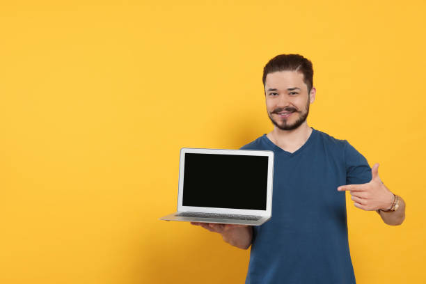 istock Emotional man pointing at laptop on orange background. Space for text 1485823813