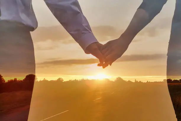 Concept of light love. Couples holding each other's hands against the backdrop of a sunny sunset with double exposure.
