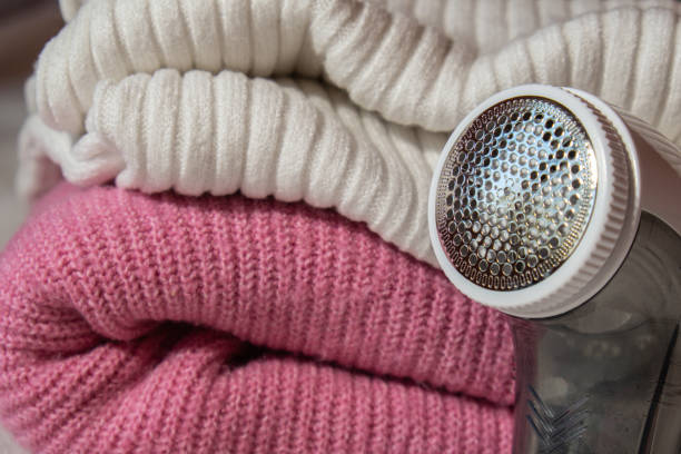 Anti-pilling razor. Device for shaving clothes. Anti-Plush fabric Shaver. Electric portable sweater pill defuzzer Lint remover from pink acrylic or wool sweater. Electric device fabric shaver after cleaning and collected fluff lint. Closeup Pilled sweater. Old used clothes with pilling. navaja anti-pilling. dispositivo para afeitarse la ropa. afeitadora de tela anti-felpa. suéter eléctrico portátil desactivador de pastillas removedor de pelusa de acrílico rosa o suéter de lana. afeitadora de telas de dispositivo eléctrico después d