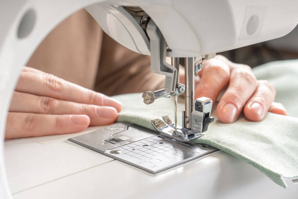 アトリエの職場で現代のミシンに白い布を縫う女性の手 - シーム ストックフォトと画像