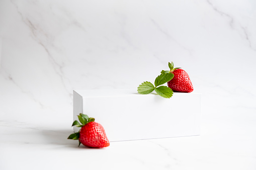 White podium with strawberry on marble background. Pedestal podium for product placement display. Trendy natural mockup template for beauty product and cosmetics scene.