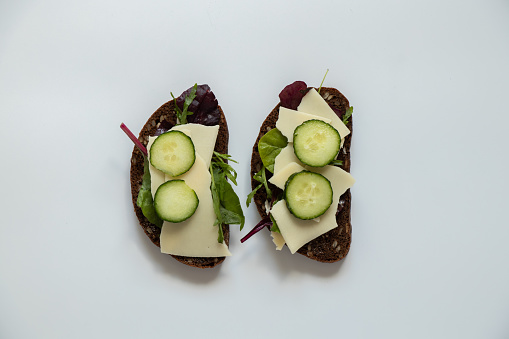 Vegetable sandwich with cheese and cucumbers and black bread with seeds on a white background, quick lunch
