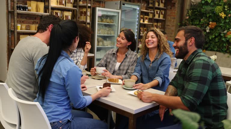 Diverse group of friends having a great time at a bakery eating and drinking coffee while laughing