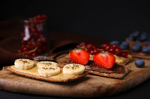 Fresh crunchy rye crispbreads with different toppings on black table, closeup